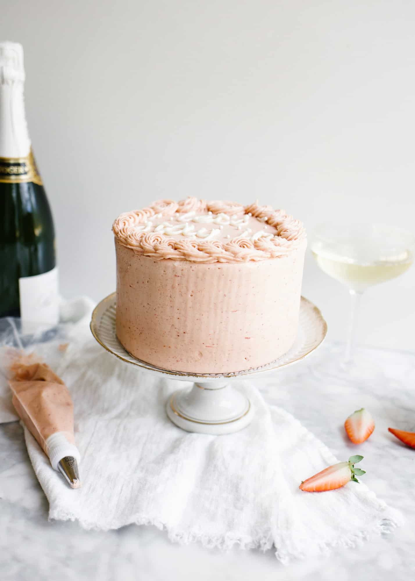 Champagne and Strawberries Cake by Wood and Spoon blog. This is a simple champagne scented layered cake topped with a real strawberry American buttercream and made extra moist with a champagne simple syrup. Two layers make up this small 6" cake which is perfect to gift or share with a valentine. Learn how to make this romantic date night in cake on thewoodandspoon.com