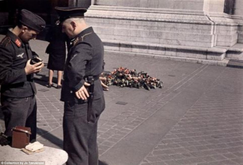 Relaxed: Rather than appear invaders, these Nazi soldiers fiddle with a camera like tourists and appear to be have a guidebook lying nearby 