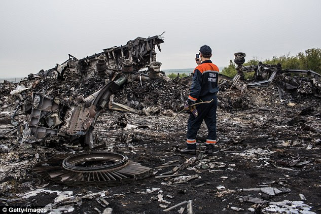 Horrific: An emergency services worker photographs debris from the Malaysia Airlines crash site after it was shot down over east Ukraine, 40km from the Russian border, in July 2014