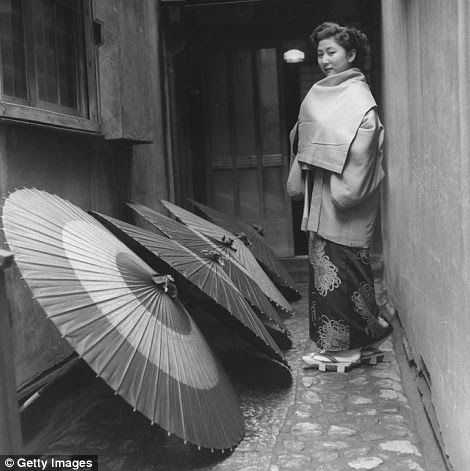 A geisha going home and passing a line of drying umbrellas in the alleyway