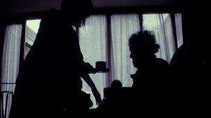 A silhouette image of a woman passing a cup of tea to an elderly lady.