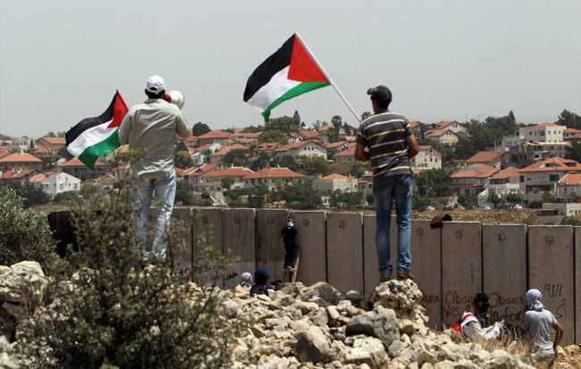 NILIN : Palestinian protesters wave the national flag as their comrades climb Israel's controversial separation barrier during clashes with Israeli security forces following a demonstration against Israeli settlements and its separation wall, in the West Bank village of Nilin near the Jewish settlement of Hashmonaim (background), on May 31, 2013. AFP PHOTO/ ABBAS MOMANI NILIN : Palestinian protesters wave the national flag as their comrades climb Israel's controversial separation barrier during clashes with Israeli security forces following a demonstration against Israeli settlements and its separation wall, in the West Bank village of Nilin near the Jewish settlement of Hashmonaim (background), on May 31, 2013. AFP PHOTO/ ABBAS MOMANI