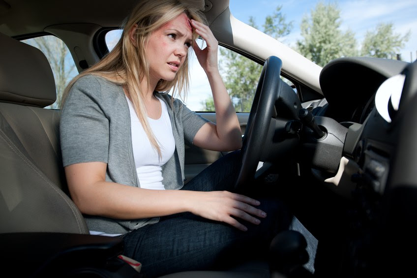 Woman has just hit her head on the steering wheel during a collision and looks up, dazed and confused, trying to figure out what just happened. She is in pain and touches at her forehead where there is a nasty impact wound and bruising. Very realistic FX make-up.