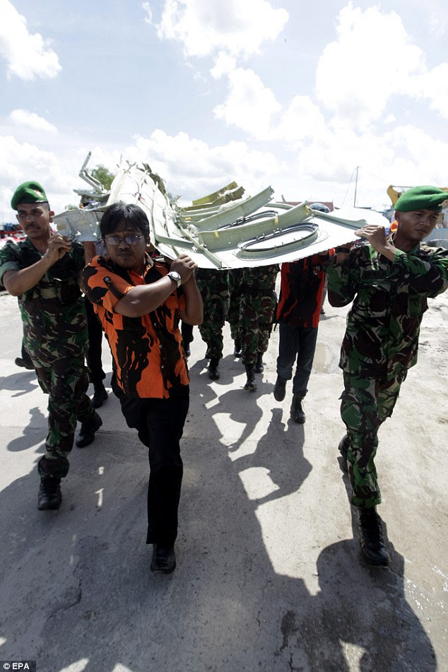 Indonesian officers carry a part of the tail section of the AirAsia plane away to be scrutinized 