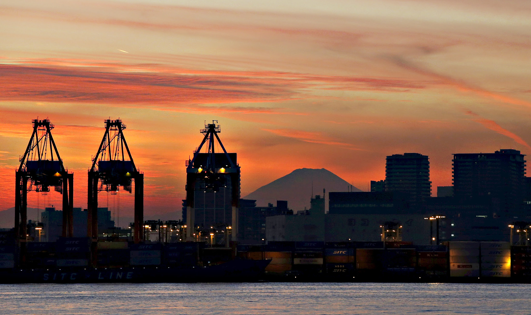 Mount Fuji is seen between cranes and buildings during sunset at a port in Tokyo, Japan, on Wednesday. Japan's core machinery orders unexpectedly jumped in October by the most since March 2014