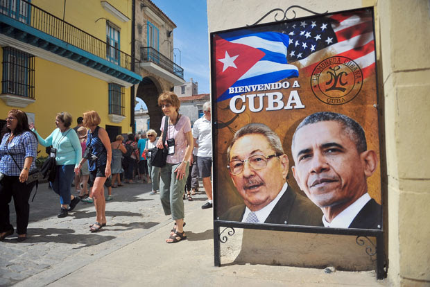 TOPSHOT - Tourists walk next to a poster of Cuban President Raul Castro and US president Barack Obama in Havana, on March 18, 2016. US president Barack Obama touches down in Havana on Sunday to cap a long-unimaginable rapprochement with Cuba and burnish a presidential legacy dulled by Middle East quagmires and partisan sniping. As Air Force One rolls to a stop, Obama will become the first sitting US president to visit Cuba since Calvin Coolidge arrived on a battleship in 1928, before the discovery of penicillin or invention of the ballpoint pen. AFP PHOTO/YAMIL LAGE / AFP PHOTO / YAMIL LAGE ORG XMIT: HAV17
