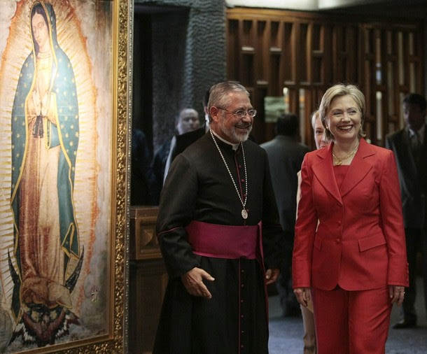 US Secretary of State Clinton smiles with priest Monrroy in front of an image of the Virgin of Guadalupe inside the Basilica de Guadalupe in Mexico City