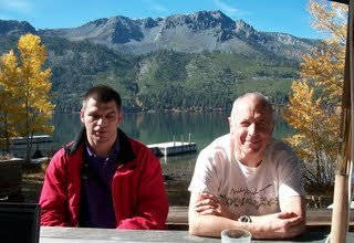 Tech support in action: Chris and Gil sitting at a picnic table with the lake and mountains in the background