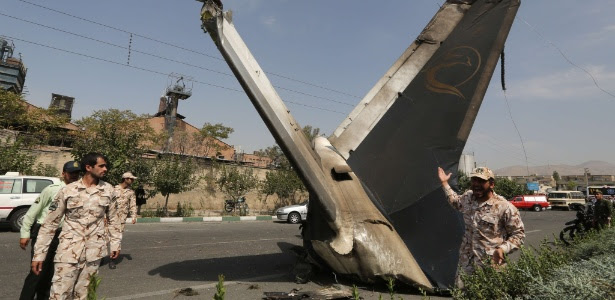 Integrante da Guarda Revolucionária do Irã observa parte de avião que caiu perto do aeroporto de Teerã
