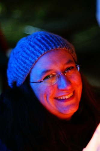Me smiling, wearing a grey knitted hat. My face is yellow and red on the side lit by the lantern, and blue on the shadow side