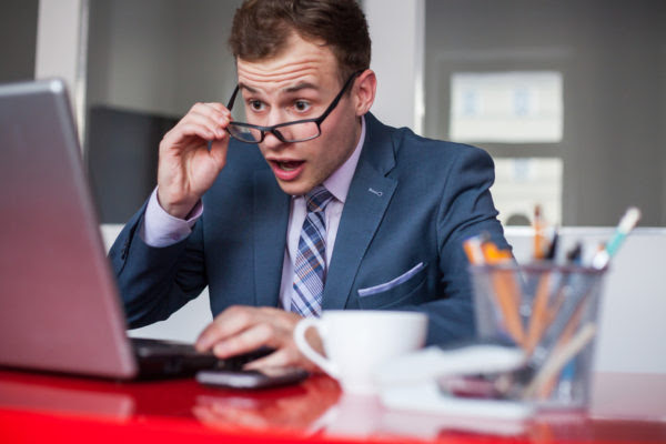 Young businessman working in bright office, sitting at desk with laptop. Expression of emotions.