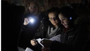 Three poll workers try to start an optical scanner voting machine Tuesday in the cold and dark at a polling station in a tent in the Midland Beach section of Staten Island, New York after the original polling site, a school, was damaged by superstorm Sandy.