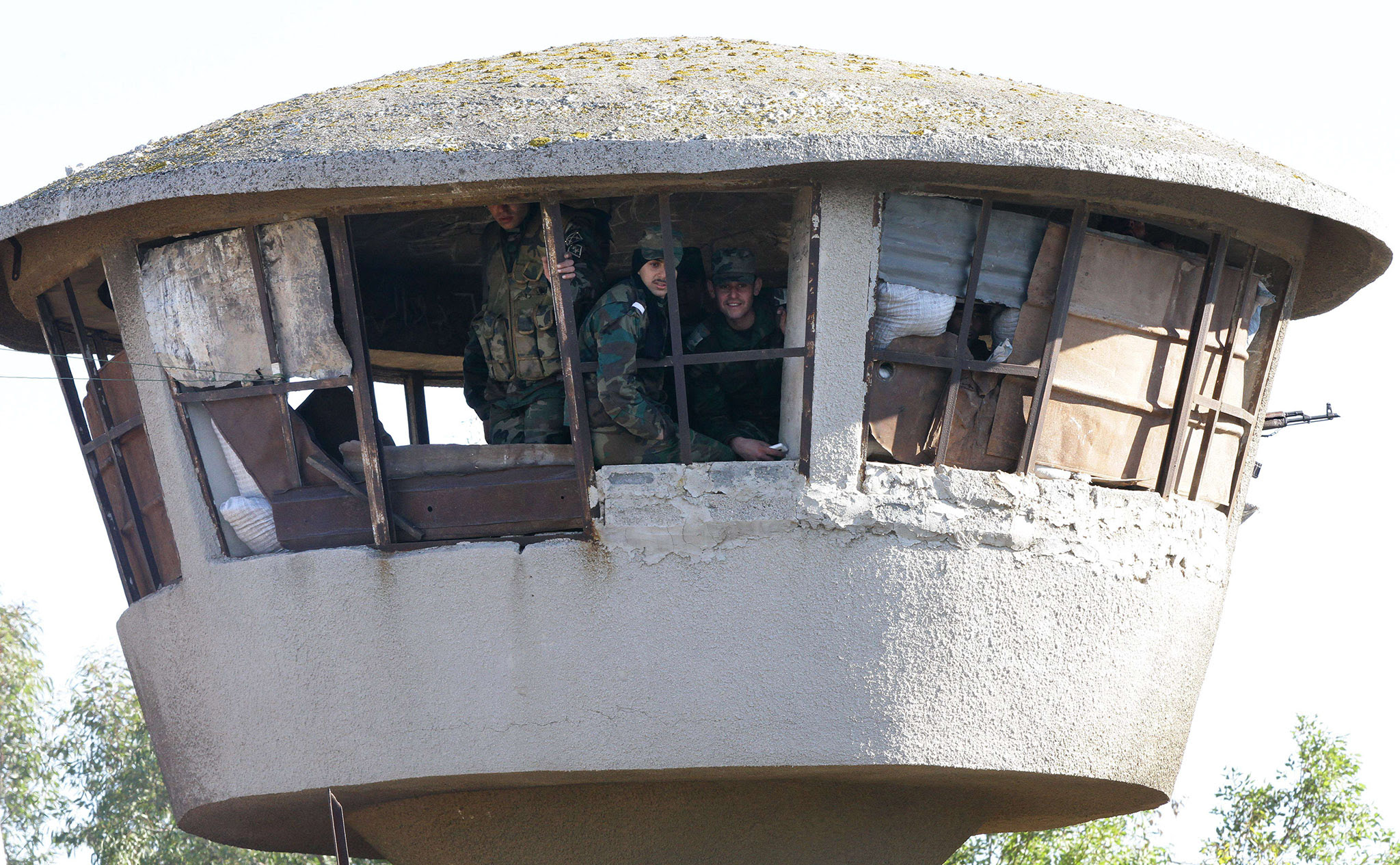Members of the Syrian government forces sit in a tower at a military base as hundreds of civilians and Syrian rebel forces began evacuating the last opposition-held district of Waer in the central city of Homs