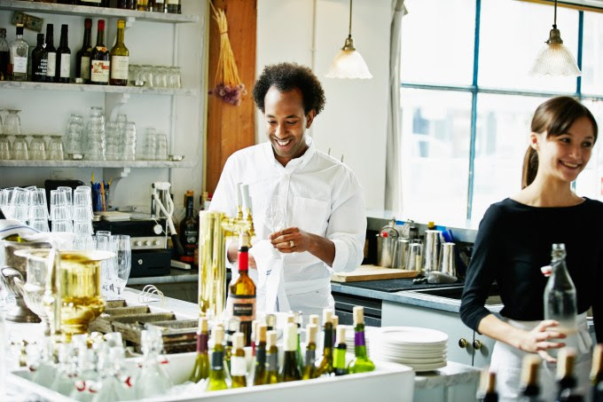Smiling waitress and bartender standing behind bar in restaurant preparing for dinner service