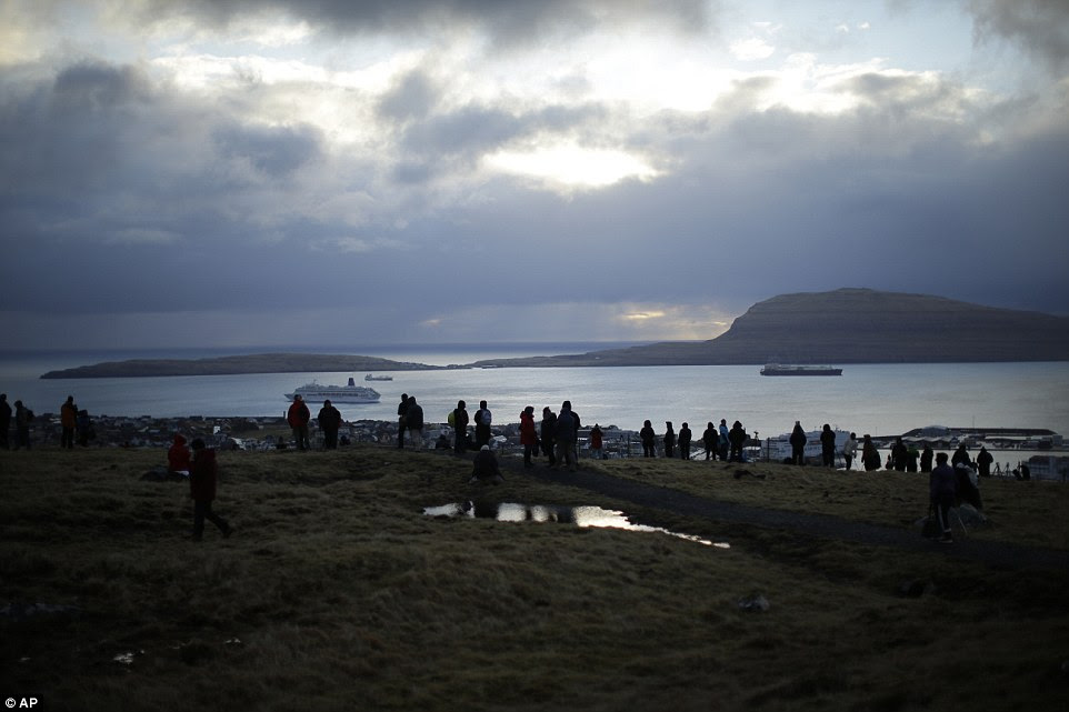 People wait for the start of a total solar eclipse from a hill beside a hotel overlooking the sea and Torshavn, the capital city of the Faeroe Islands