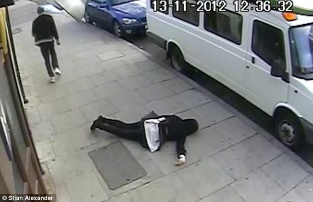 Out cold: The 16-year-old lies stricken and unmoving on the pavement as the attacker walks nonchalantly away