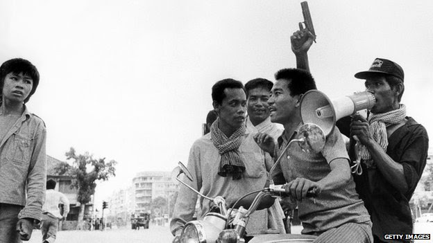 A Khmer Rouge guerrilla soldier holding a gun rides a motorcycle while he and his fellow comrade enter Phnom Penh on 17 April 1975 