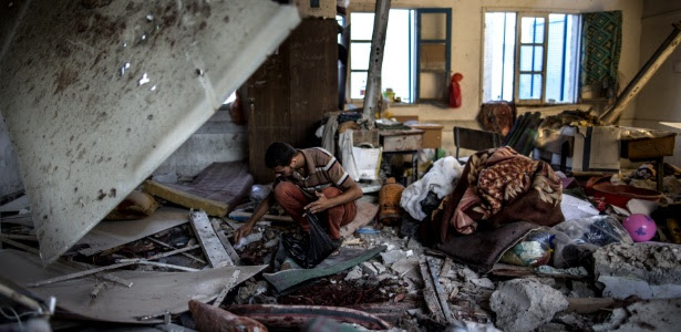 Observador palestino recolhe restos em sala de aula de escola da ONU bombardeada em Gaza. A instituição mantida pela UNRWA (Agência das Nações Unidas de Assistência aos Refugiados da Palestina funcionava como abrigo para refugiados