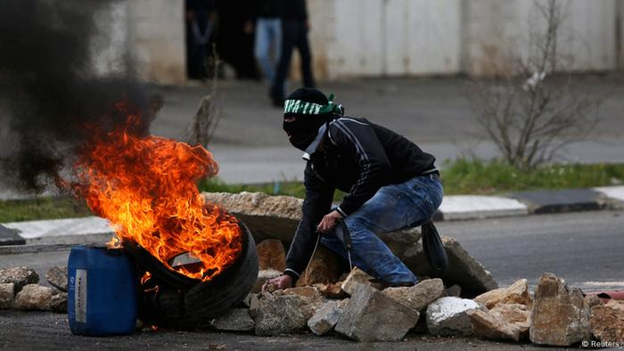 A stone-throwing Palestinian protester crouches near burning tyres during clashes with Israeli soldiers and border policemen outside Israel's Ofer military prison near the West Bank city of Ramallah February 24, 2013. Israel on Sunday demanded the Palestinian Authority stem a surge of anti-Israeli protests ahead of U.S. President Barack Obama's visit to the region next month. The death in an Israeli jail of a Palestinian detainee on Saturday and an on-going hunger strike by four inmates have fuelled tensions in the West Bank. REUTERS/Mohamad Torokman (WEST BANK - Tags: POLITICS CIVIL UNREST)