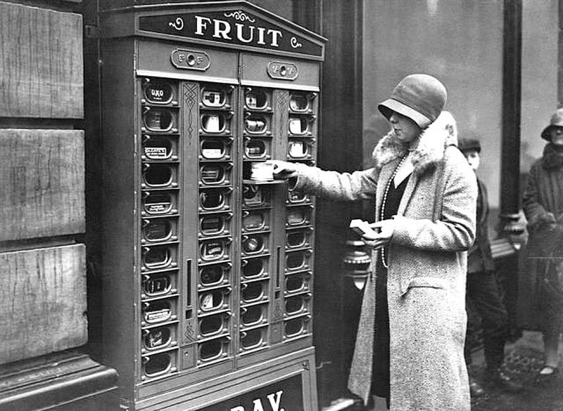 Торговый автомат в Англии в 1920 году, который распределяет фрукты, кубики Oxo, другие банки с продуктами питания, спички и продукты Colgate. история, черно-белая фотография, юмор