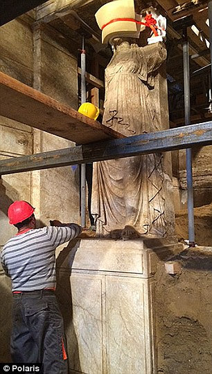 an expert works on painstakingly removing the soil surrounding a large sculpture of a Caryatid