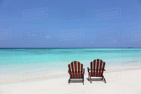 Two adirondack chairs on sunny, tranquil beach overlooking 