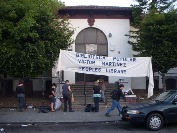 A small group of activists in front of the library with banner reading Biblioteca Popular Victor Martinez People's Library