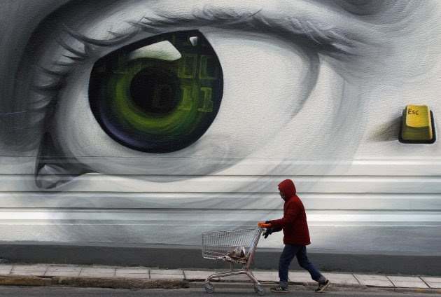 An immigrant pushes an empty shopping trolley past graffiti in Athens