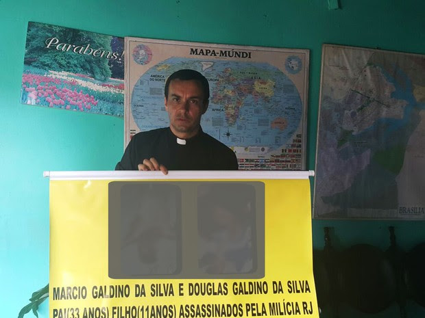 O padre polonês Pedro Stepien, que afirma ser alvo de ameaças de milícias do RJ, segurando banner com fotos de vítimas (Foto: Raquel Morais/G1)