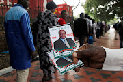 A man hold pictures of the former Kenya's President Mwai Kibaki as he waits in line to pay his respects, during a public display of his body at the House of Parliament in Nairobi, Kenya, April 26, 2022. 