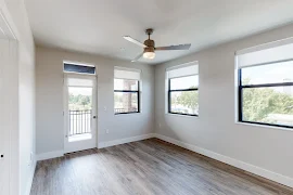 Living room with wood-inspired flooring, ceiling fan, windows, and door to the balcony