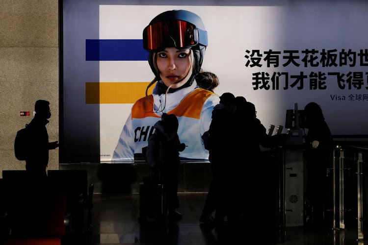 People line up to board a train near an image of freestyle skier Eileen Gu at a railway station at the Beijing 2022 Winter Olympics