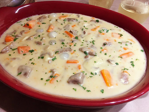 A serving dish with meat, carrots and pearl onions in a white sauce.