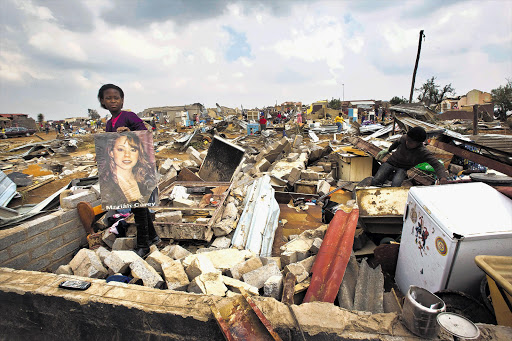 A young girl recovers her Mariah Carey poster from where her room used to be after a tornado hit Duduza township, near Nigel, killing one person and injuring more than 100. File photo.