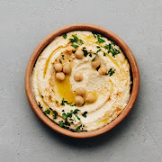 Large bowl of homemade hummus garnished with chickpeas, red sweet pepper, parsley and olive oil.