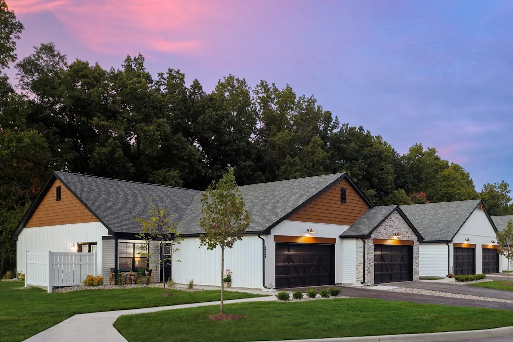 Apartment homes with white and brown siding backed by trees at dusk