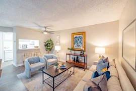 Model living room with furniture, wood inspired flooring, neutral beige walls, white trim, and a ceiling fan