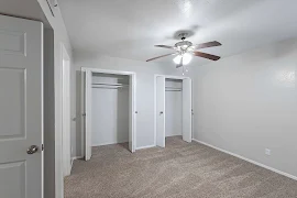 Bedroom with neutral walls & carpet with light trim, and two closets with bifold doors with hanging rods & upper shelves.