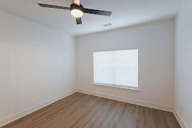 Bedroom with large window with blinds, wood plank flooring, white walls and trim, and a ceiling fan