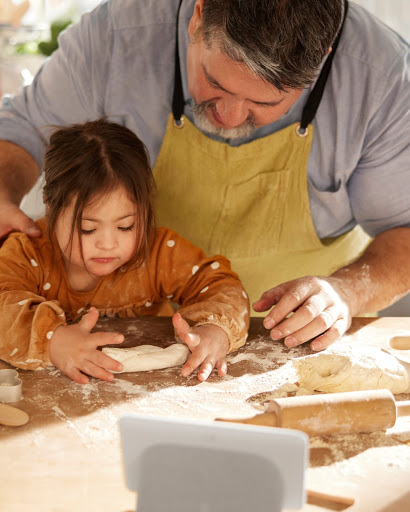 Vue en plongée sur les mains d'un homme qui montre à sa fille comment étaler de la pâte avec un rouleau à pâtisserie.