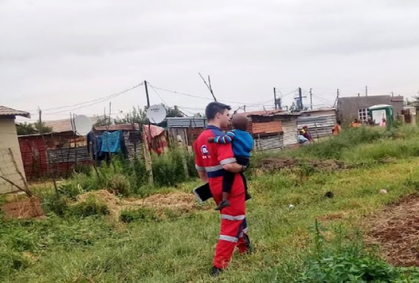 A paramedic carries the child who was found safe after being left in his father's hijacked car.