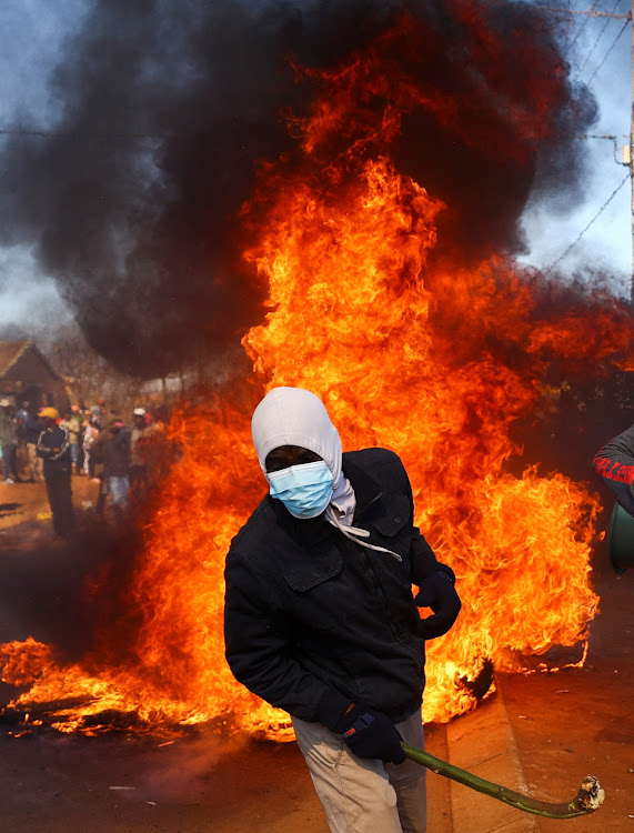 A man holding a stick reacts next to a fire after community members burned shacks and belongings as they searched for alleged illegal miners known as ‘zama-zamas’ as a protest, following alleged rape of eight models on July 28 when a television crew filmed a music video at a mine dump in the nearby township, in the West Rand, South Africa, on August 8, 2022.