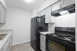 Modern kitchen in an apartment featuring black appliances, grey cabinets, and stone-style countertops.