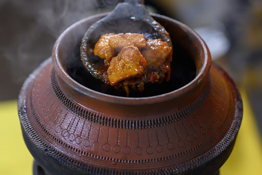 Cooked chicken pieces can be seen being lifted out of a clay vessel during the cooking of Sohbat (Flatbread and chicken stew) in Khanewal