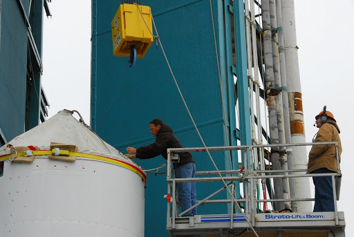 Spacecraft technicians prepare to attach the interstage of the United Launch Alliance Delta II Operational Environmental Satellite System Preparatory Project.