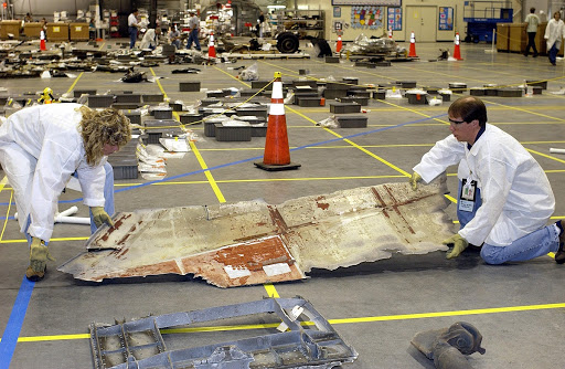 Two members of the Columbia Reconstruction Project Team place a piece of Columbia debris on the floor of the RLV Hangar at KSC.