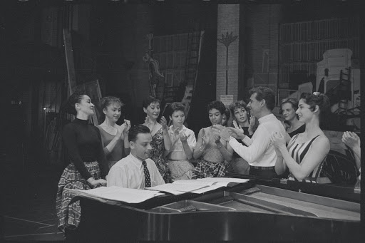 Chita Rivera, Stephen Sondheim, Leonard Bernstein, Carol Lawrence, and cast around piano in rehearsal for the stage production West Side Story