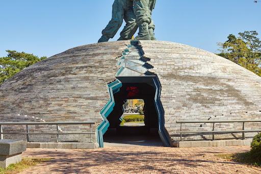 This work depicts the dramatic reunification of brothers fighting in the Korean War, one an officer with the Korean Army and the other a North Korean soldier. The brothers’ embrace signifies reconciliation, love, and forgiveness amid the tragic fratricide of the Korean War. The base is in the shape of an ancient burial mound, made with granite blocks collected from all over the peninsula. It represents the Koreans’ longing to see the nation and country reunited. The dome is split into halves at the bottom, and the halves become united toward the top of the structure. This too is symbolic of the reunification of Korea.