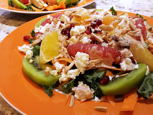 An orange plate filled with segments grapefruit, mandarin and orange, and topped with cheese.