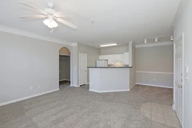 Living room facing kitchen and dining area with ceiling fan and neutral colored carpet and walls